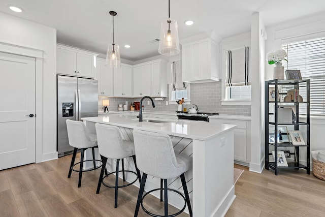 kitchen with stainless steel fridge, a center island with sink, light countertops, light wood-type flooring, and a sink