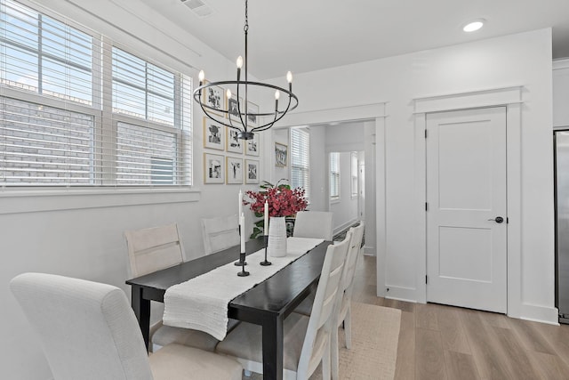 dining space with a healthy amount of sunlight, light wood-style flooring, visible vents, and a notable chandelier