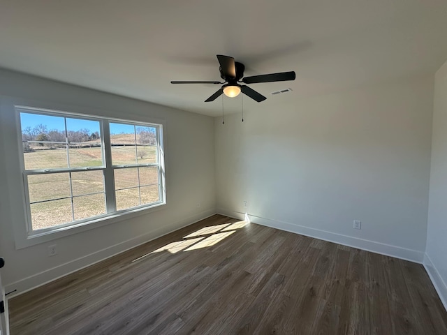 spare room with dark wood-type flooring, a ceiling fan, visible vents, and baseboards