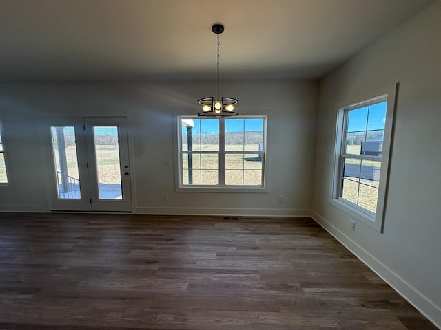 unfurnished dining area featuring an inviting chandelier, baseboards, and dark wood-type flooring