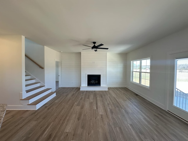 unfurnished living room featuring a large fireplace, stairs, baseboards, and dark wood-style flooring