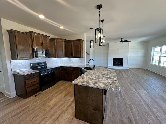 kitchen with stainless steel microwave, electric range, a sink, light stone countertops, and a peninsula