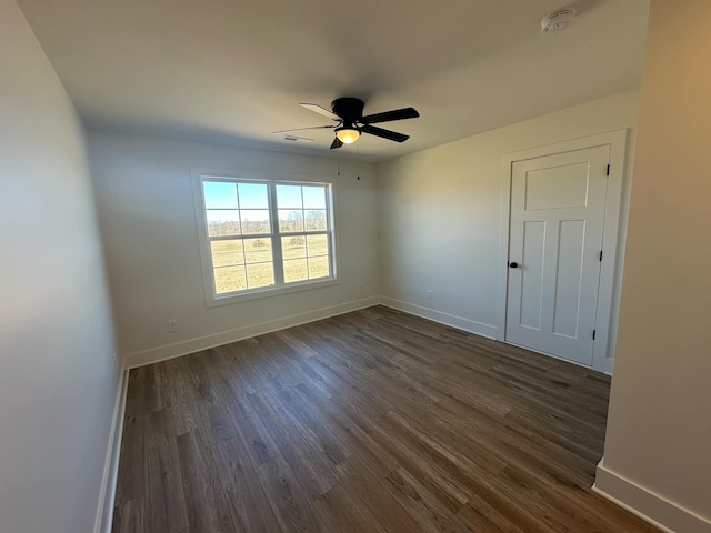 unfurnished room with dark wood-style flooring, a ceiling fan, and baseboards