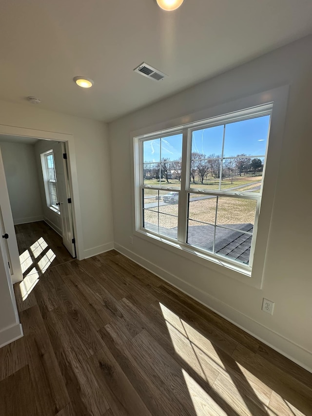 spare room with dark wood-type flooring, visible vents, and baseboards