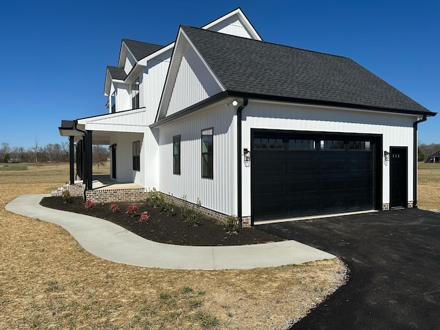 view of side of property featuring a garage, driveway, a porch, and roof with shingles