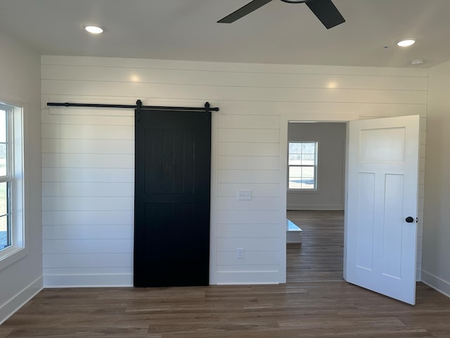 unfurnished bedroom with recessed lighting, dark wood finished floors, baseboards, and a barn door