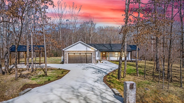 view of front of property featuring driveway, a view of trees, an attached garage, board and batten siding, and brick siding