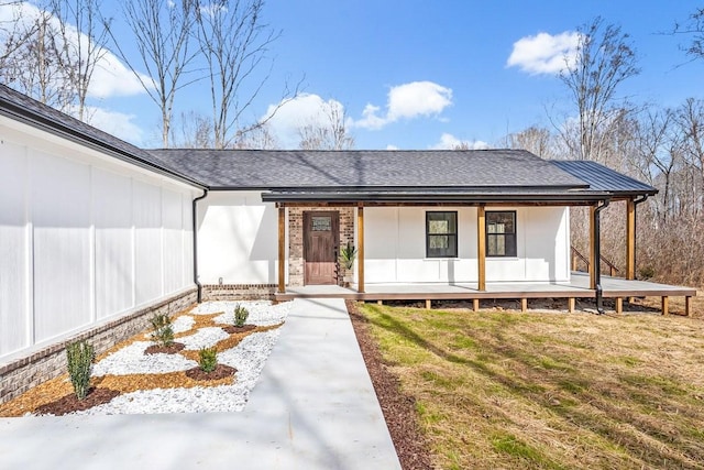 exterior space with covered porch, brick siding, a front lawn, and a shingled roof