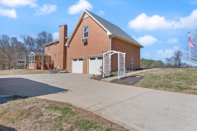 view of side of home with an attached garage, a chimney, concrete driveway, and brick siding