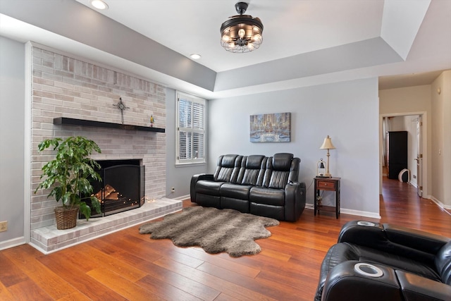 living room featuring a fireplace, baseboards, a raised ceiling, and hardwood / wood-style floors