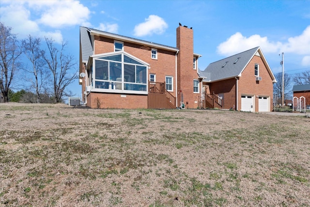 back of house featuring central air condition unit, a garage, brick siding, a sunroom, and a chimney