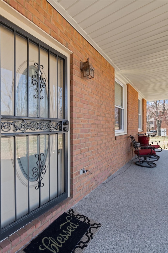 view of exterior entry featuring covered porch and brick siding