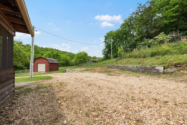 view of yard featuring a garage, dirt driveway, an outbuilding, fence, and a wooded view