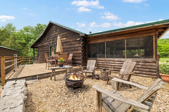 exterior space featuring a sunroom, log exterior, a fire pit, and a wooden deck