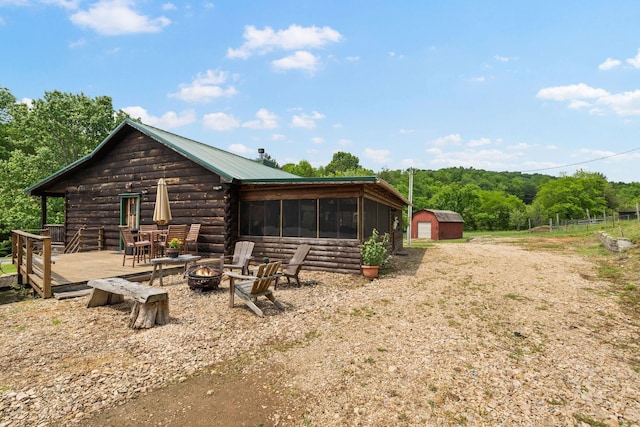 rear view of house with metal roof, a fire pit, a storage shed, an outdoor structure, and a sunroom