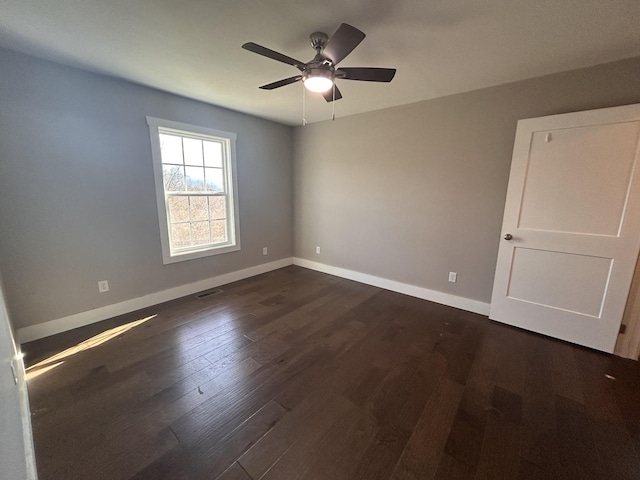 spare room featuring dark wood-style floors, visible vents, baseboards, and a ceiling fan