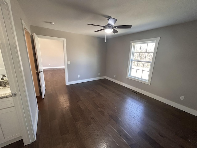 interior space featuring dark wood-style flooring, visible vents, ceiling fan, and baseboards