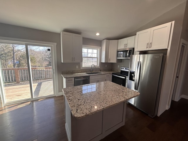 kitchen featuring dark wood finished floors, a kitchen island, light stone counters, stainless steel appliances, and a sink