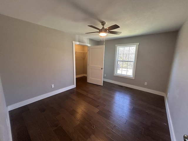 unfurnished bedroom with a walk in closet, dark wood finished floors, a closet, visible vents, and baseboards