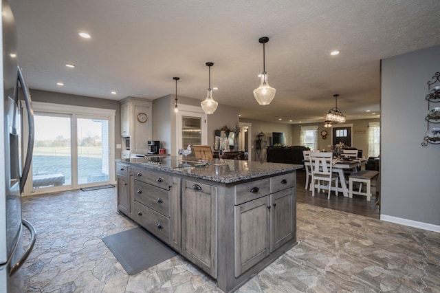 kitchen featuring dark stone counters, stainless steel fridge with ice dispenser, a kitchen island, black electric cooktop, and gray cabinets