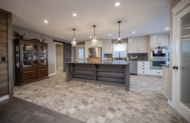 kitchen with a barn door, stainless steel appliances, white cabinets, decorative backsplash, and open shelves