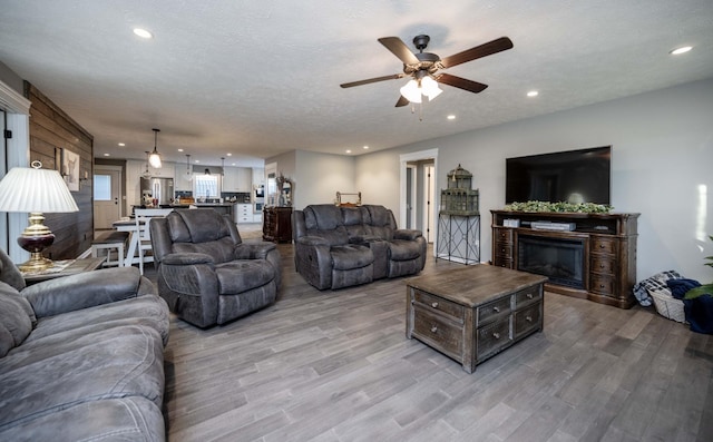 living room with a textured ceiling, recessed lighting, a ceiling fan, light wood finished floors, and a glass covered fireplace