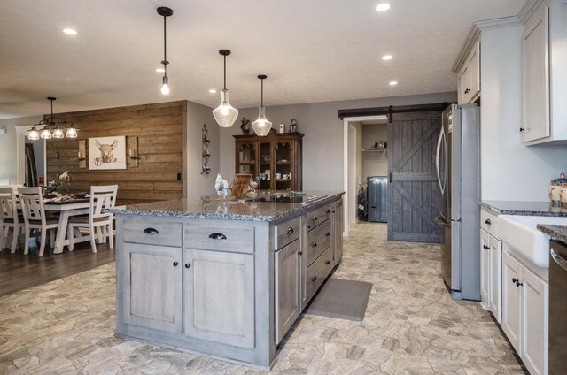 kitchen with a barn door, appliances with stainless steel finishes, a kitchen island, wooden walls, and dark stone countertops