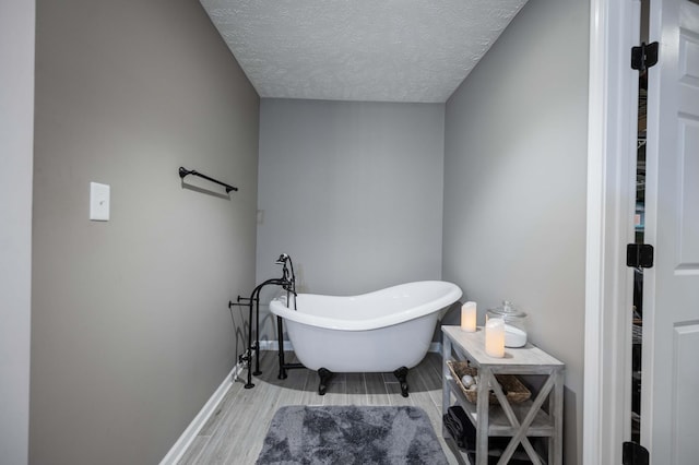 full bath with a textured ceiling, wood finish floors, a freestanding tub, and baseboards