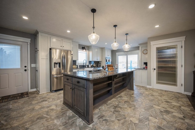 kitchen featuring a sink, a kitchen island, appliances with stainless steel finishes, open shelves, and dark stone countertops