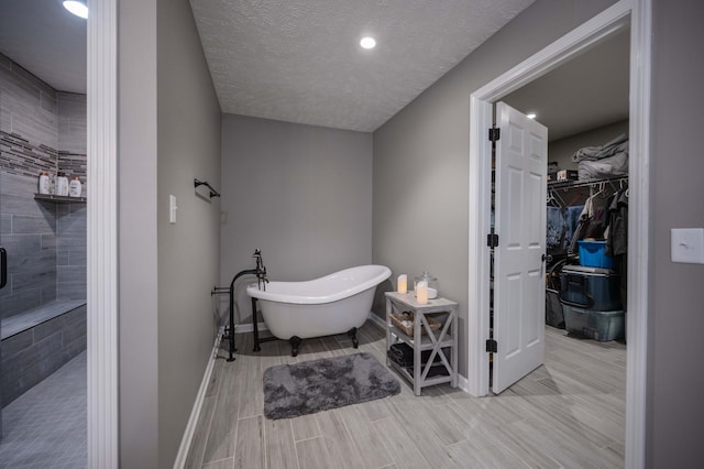 bathroom with a walk in closet, wood finish floors, a soaking tub, a textured ceiling, and baseboards