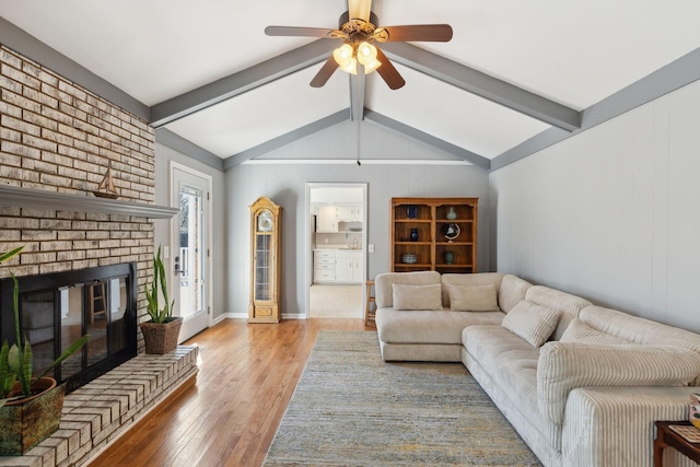 living room with baseboards, ceiling fan, wood finished floors, vaulted ceiling with beams, and a brick fireplace