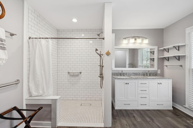 full bath with double vanity, a tile shower, a sink, and wood finished floors