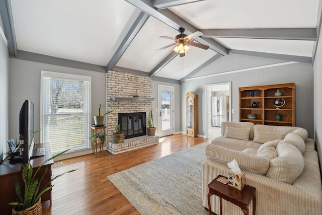 living area with vaulted ceiling with beams, ceiling fan, a fireplace, and wood finished floors