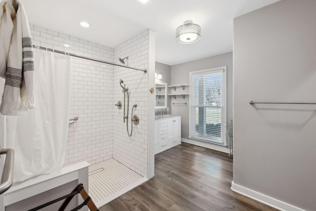 full bathroom featuring tiled shower, vanity, baseboards, and wood finished floors