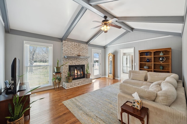 living area with lofted ceiling with beams, a fireplace, a wealth of natural light, and wood finished floors