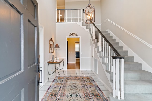 tiled entrance foyer with stairs, a high ceiling, and an inviting chandelier