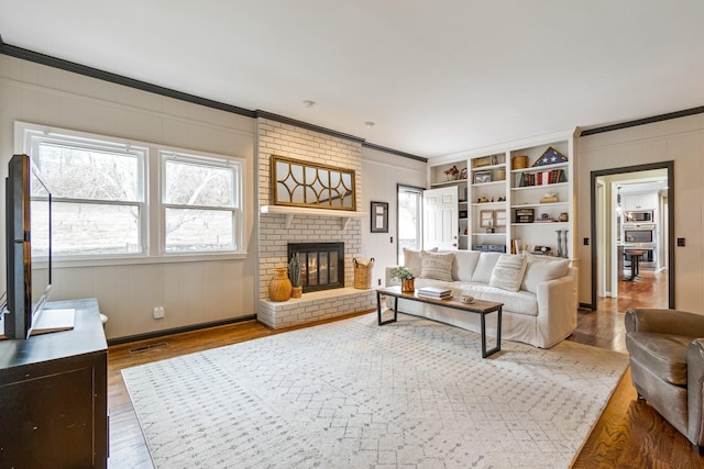 living room featuring ornamental molding, a brick fireplace, visible vents, and wood finished floors