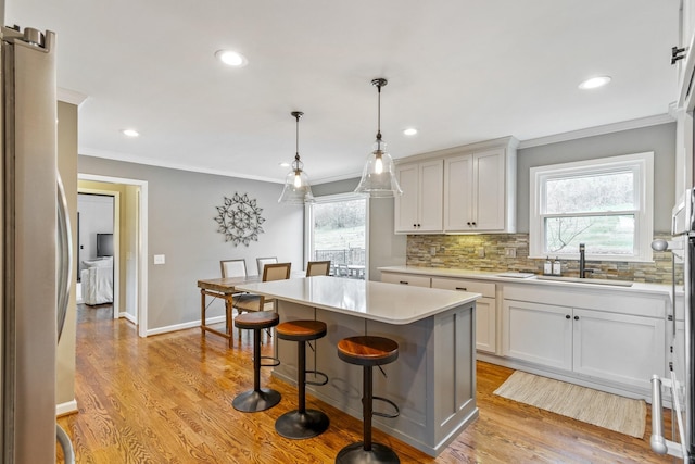 kitchen with light countertops, decorative backsplash, freestanding refrigerator, a sink, and light wood-type flooring