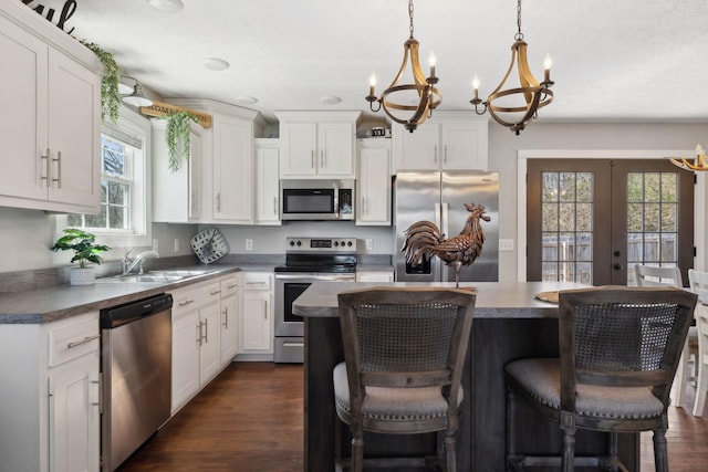 kitchen featuring dark wood-style flooring, stainless steel appliances, white cabinetry, a sink, and a kitchen island