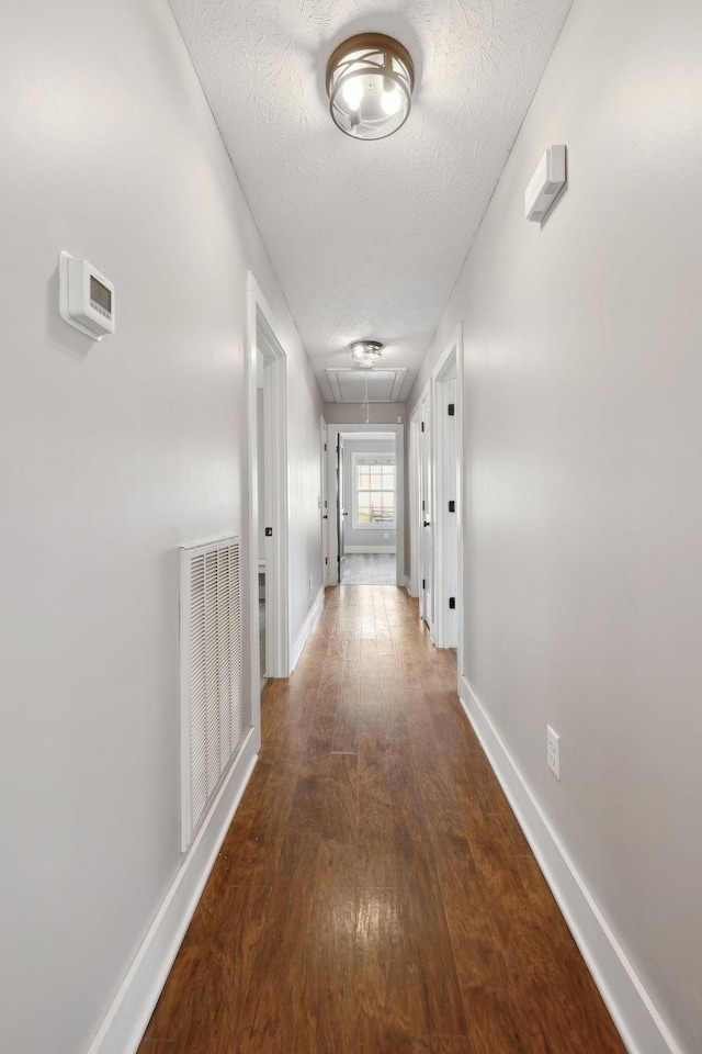 hall featuring attic access, visible vents, baseboards, dark wood-style floors, and a textured ceiling