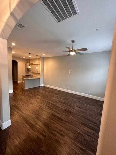 unfurnished living room with arched walkways, dark wood-style flooring, visible vents, and baseboards