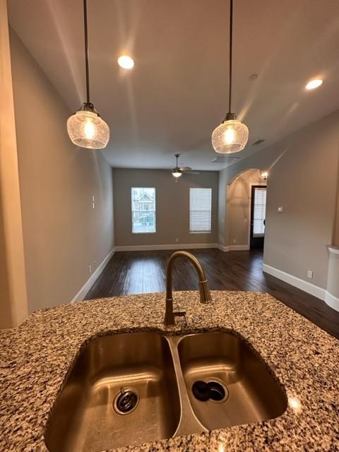 kitchen with light stone countertops, dark wood finished floors, a sink, and decorative light fixtures