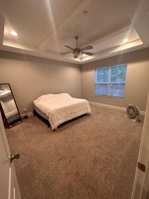 bedroom with carpet floors, a tray ceiling, and baseboards