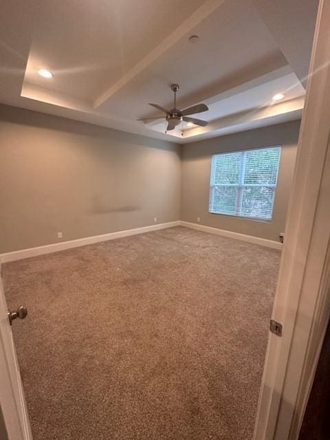 unfurnished room featuring carpet, a raised ceiling, ceiling fan, and baseboards