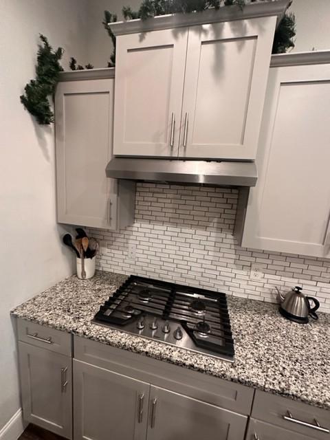 kitchen featuring under cabinet range hood, tasteful backsplash, gray cabinets, and stainless steel gas stovetop