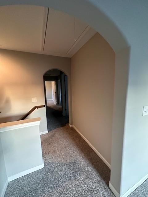 hallway featuring carpet floors, arched walkways, attic access, and baseboards