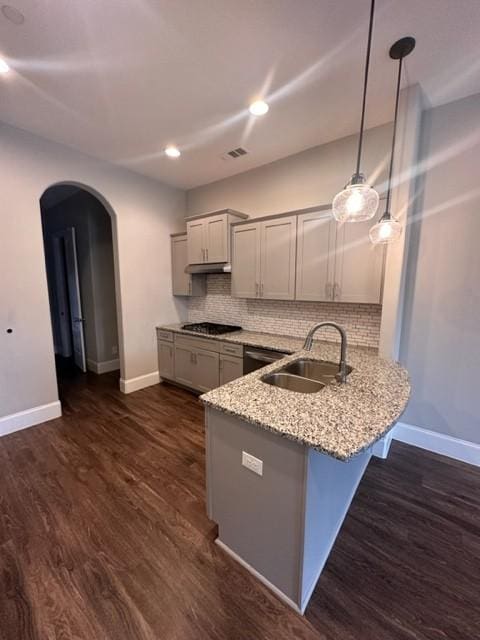 kitchen featuring arched walkways, dark wood-style flooring, a peninsula, gas cooktop, and a sink