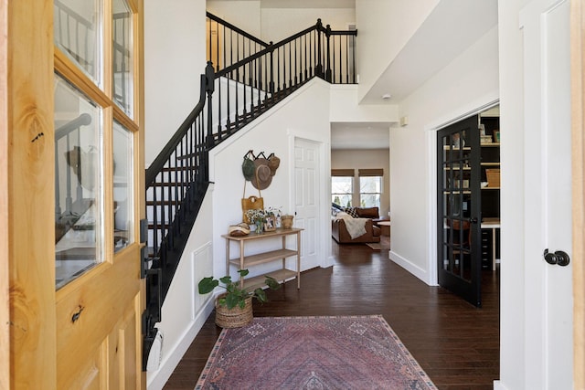 foyer entrance with a towering ceiling, baseboards, stairway, and wood finished floors