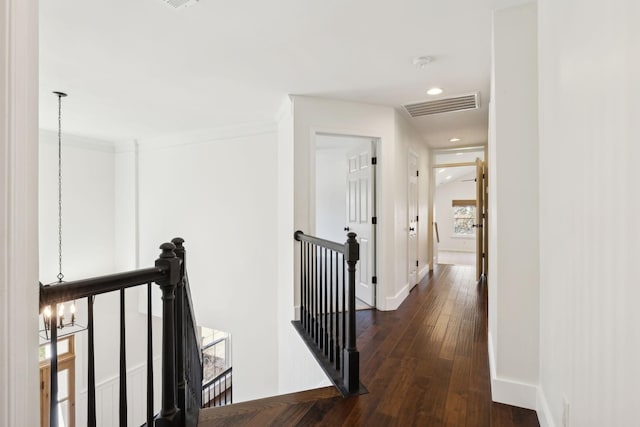 corridor with baseboards, visible vents, dark wood finished floors, and an upstairs landing