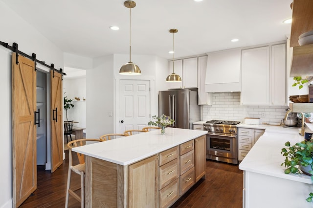 kitchen with a breakfast bar, stainless steel appliances, decorative backsplash, a barn door, and premium range hood